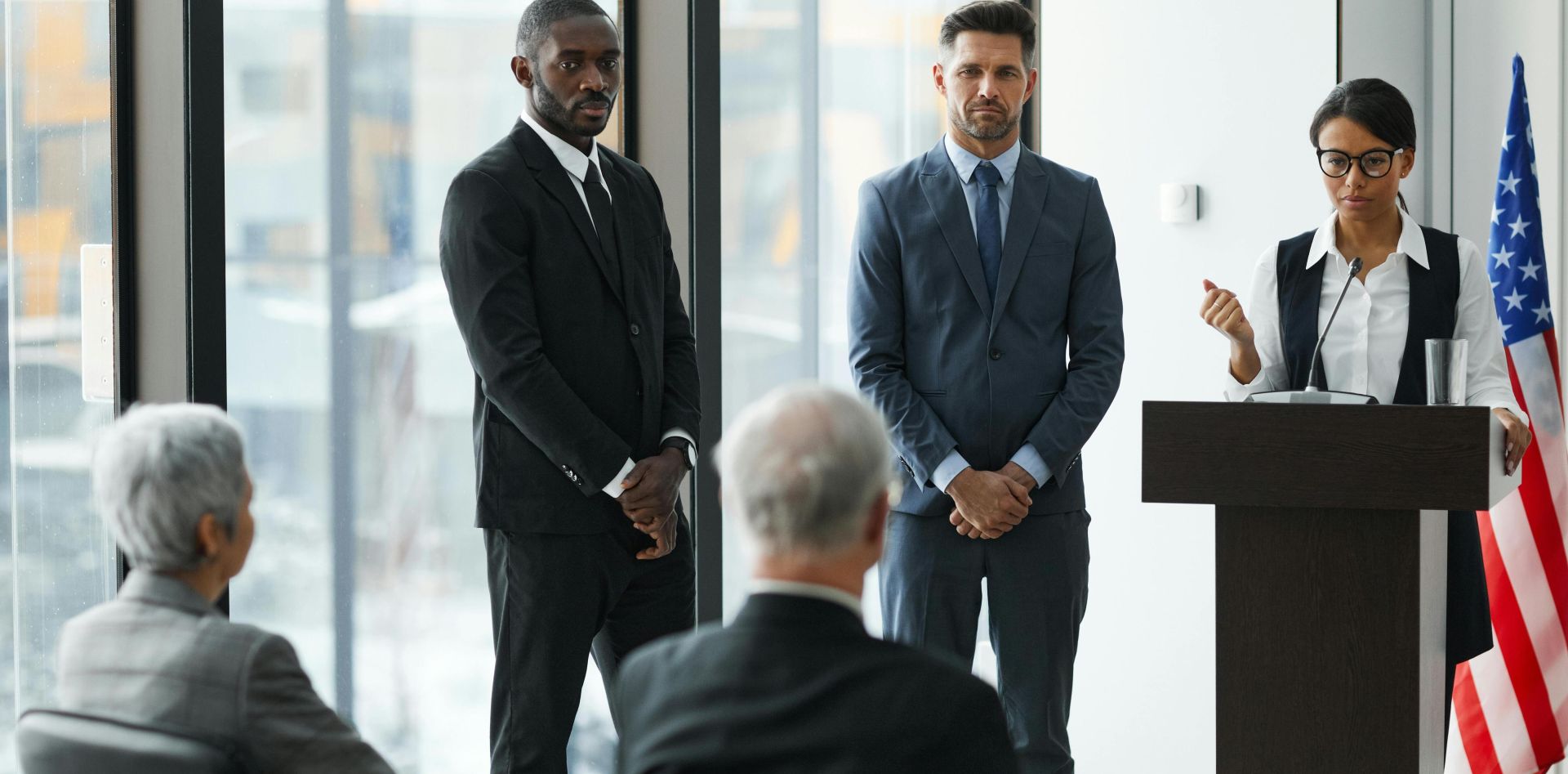 Professional speakers presenting at a conference in a modern room with glass windows.